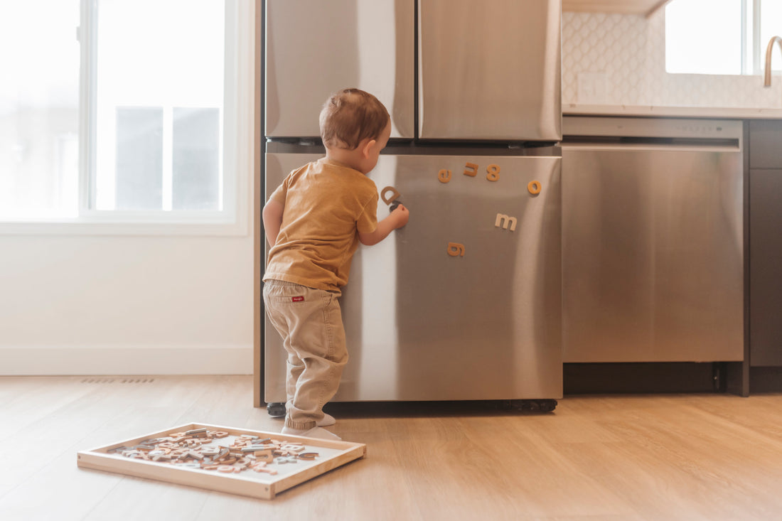toddler playing with magnetic letters on the fridge