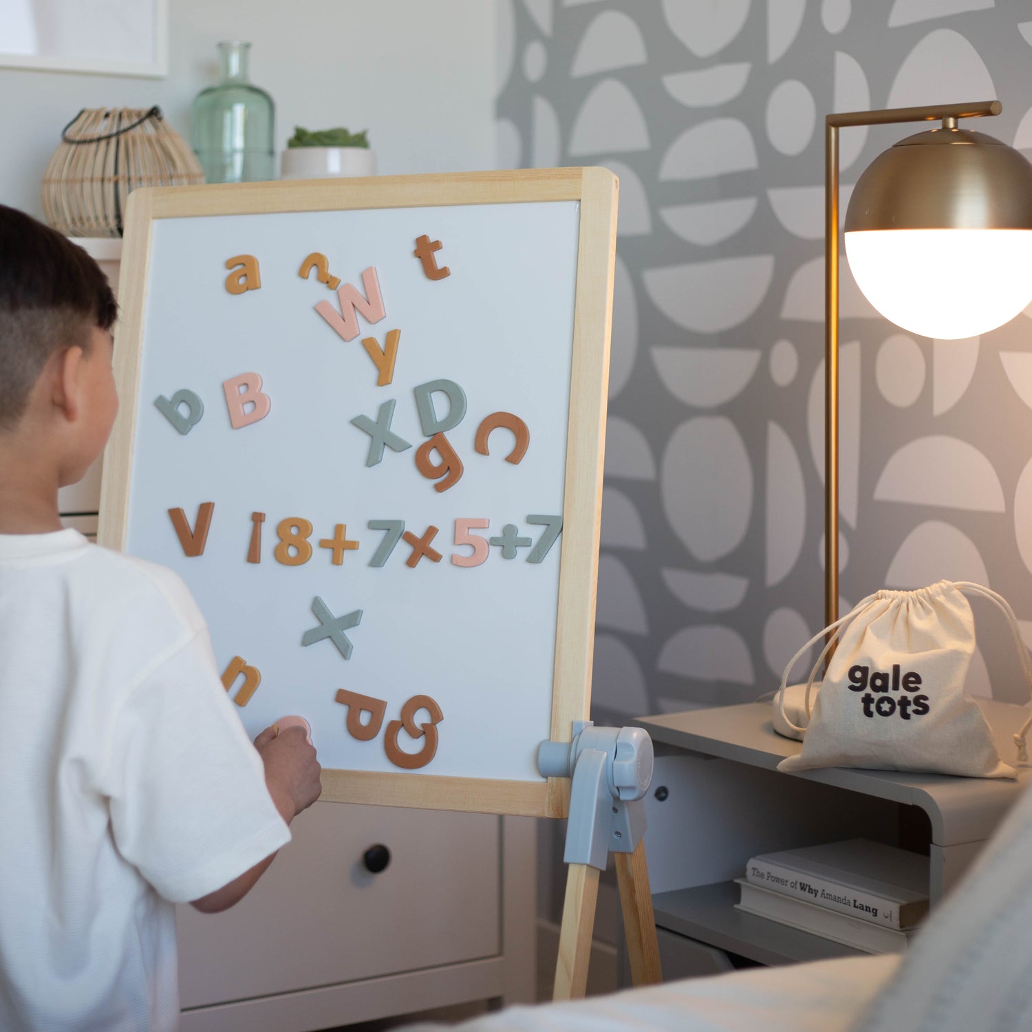 Child interacting with a whiteboard with magnetic letters and numbers in a room 