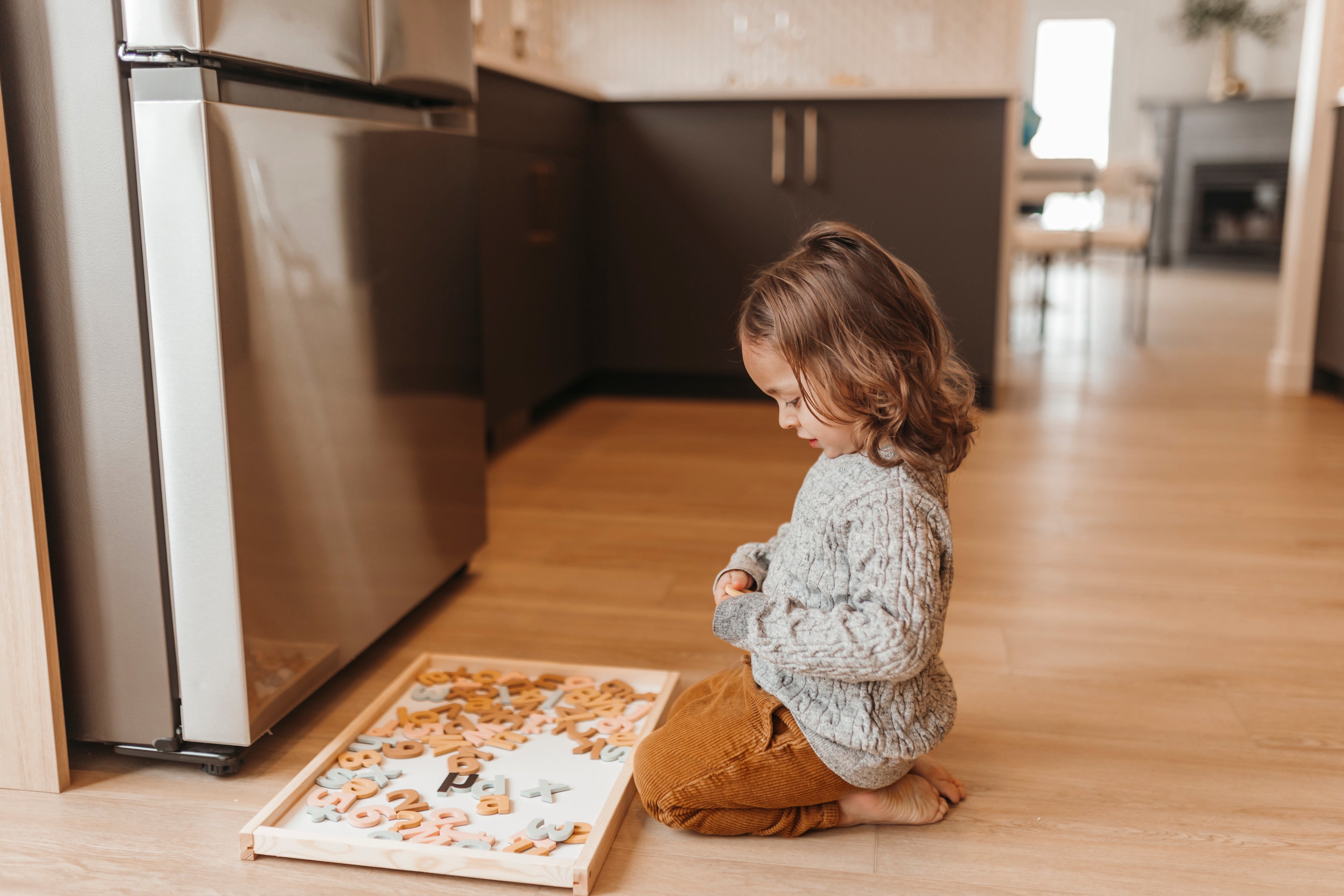 Child playing with aesthetic magnetic letters on the floor in a kitchen