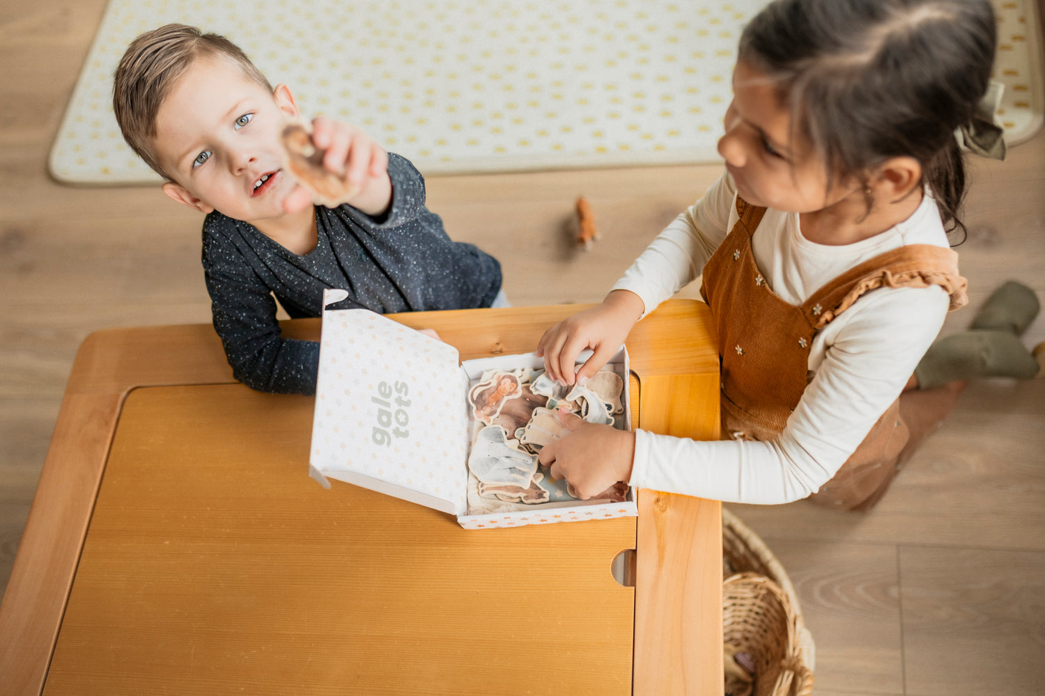 Two children sitting at a table with a book, engaged in reading or playing.