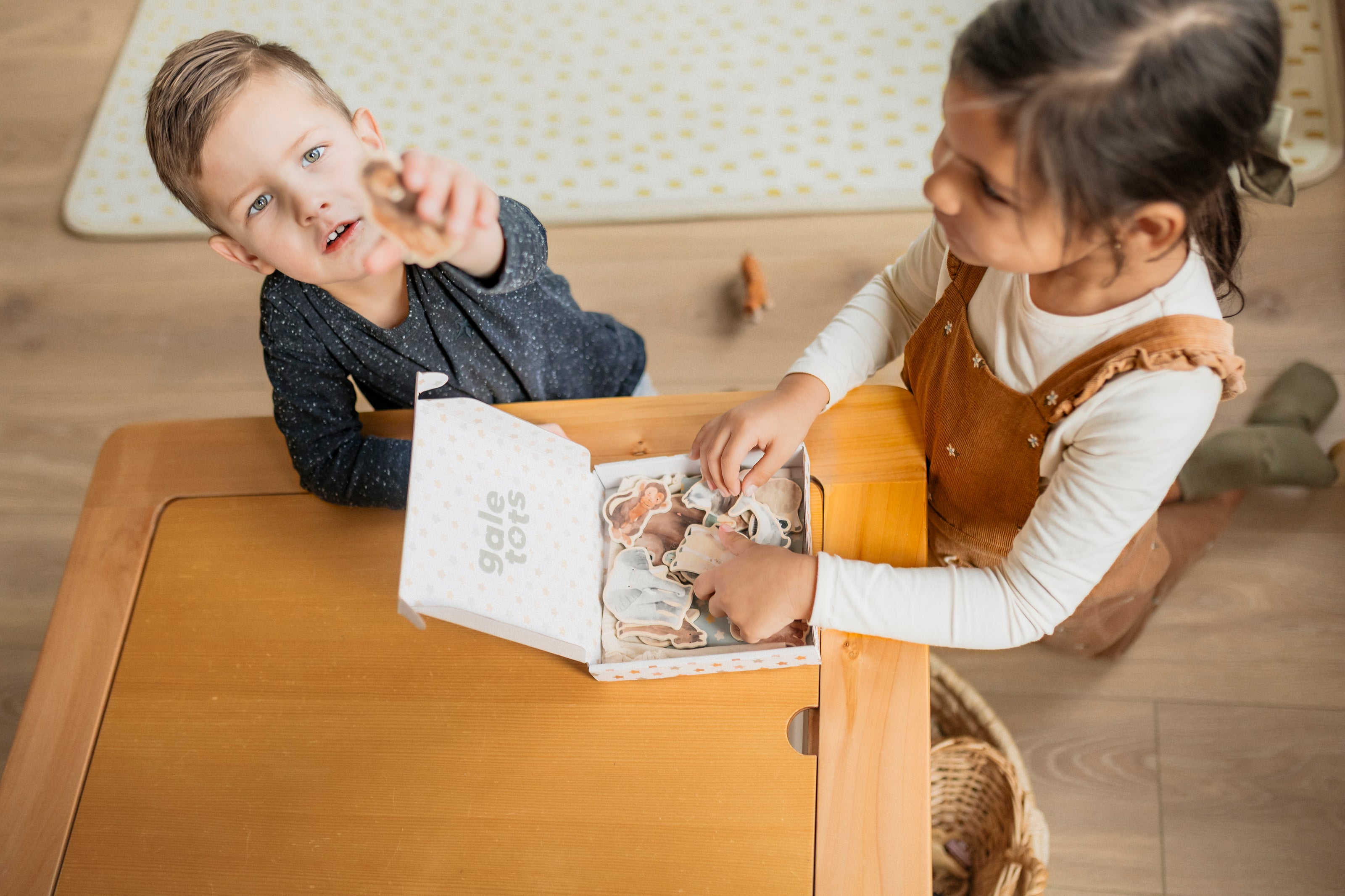 Two children sitting at a table with a book, engaged in reading or playing.