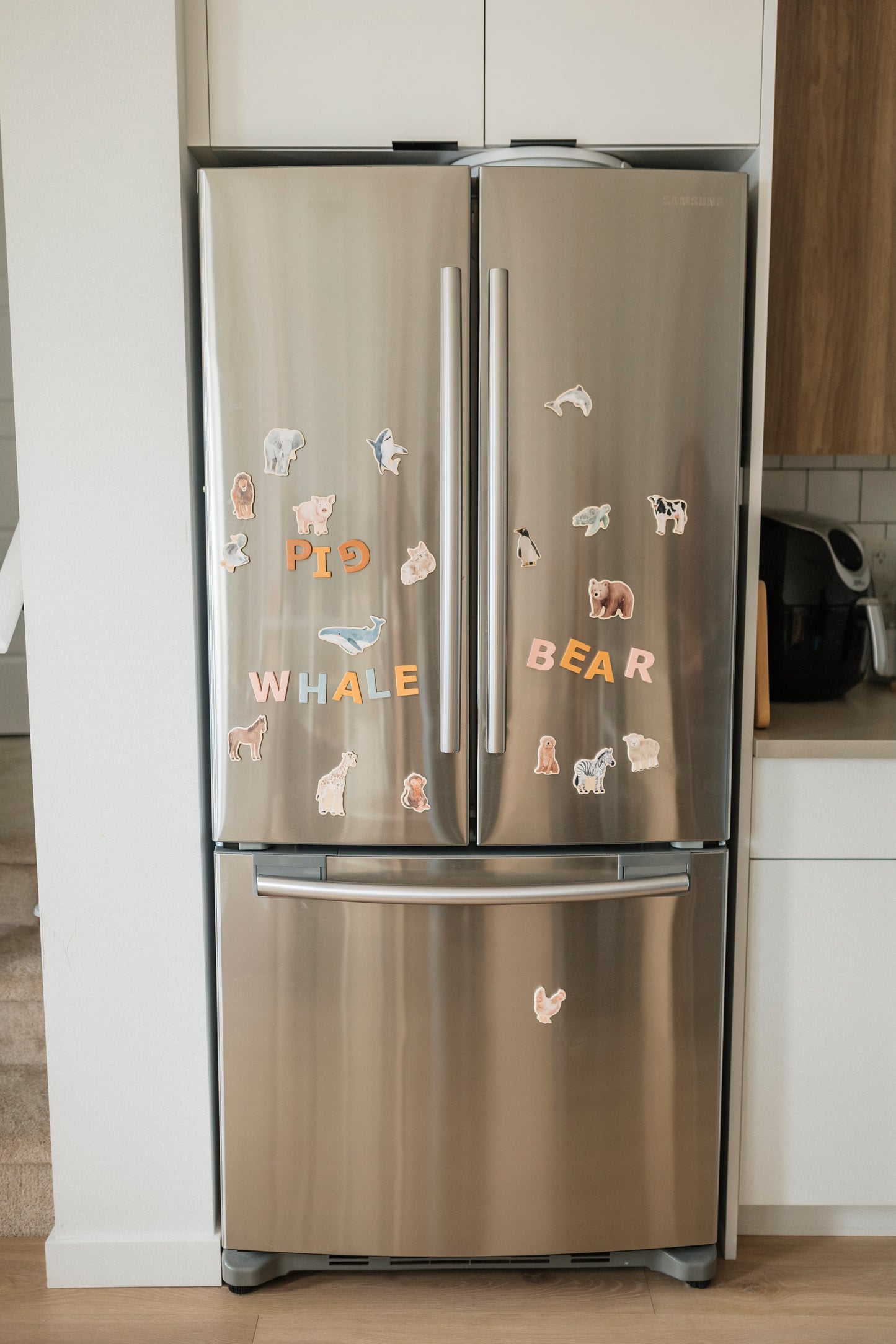 Stainless steel refrigerator with animal-themed magnets in a kitchen setting