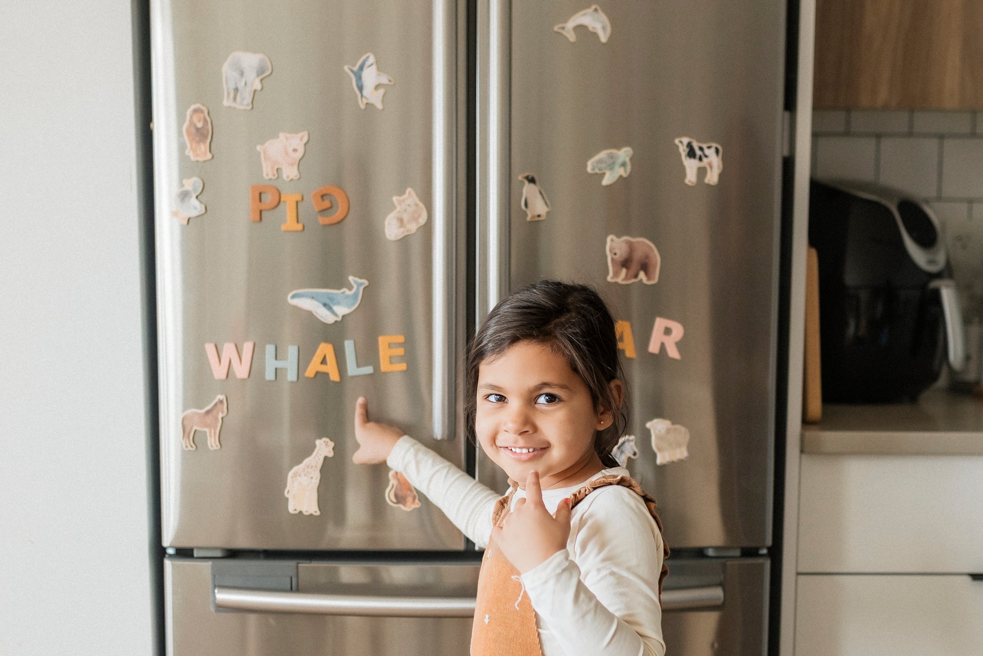 Child pointing at a refrigerator with animal and letter magnets in a kitchen