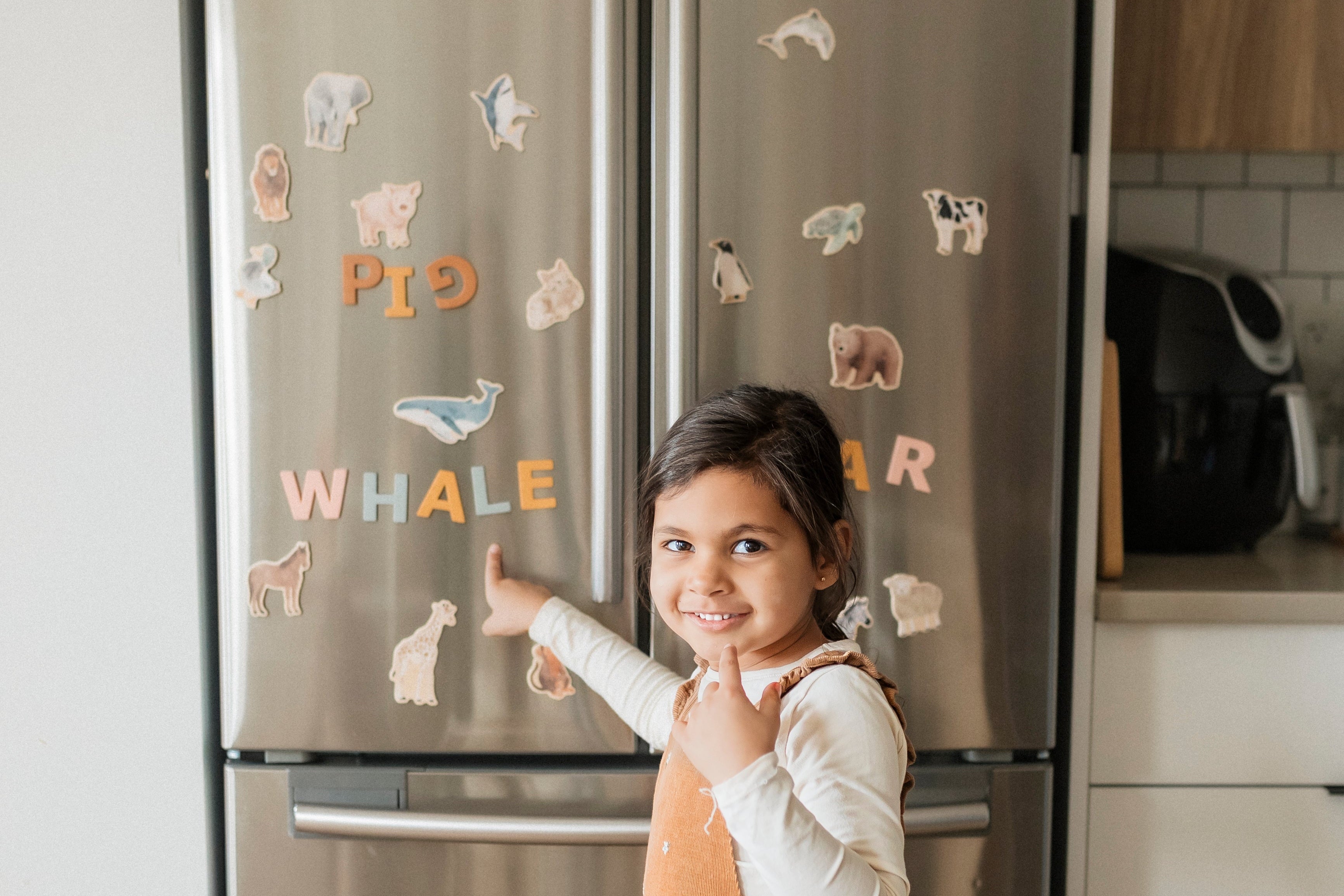 A child pointing at a refrigerator with animal magnets in a kitchen