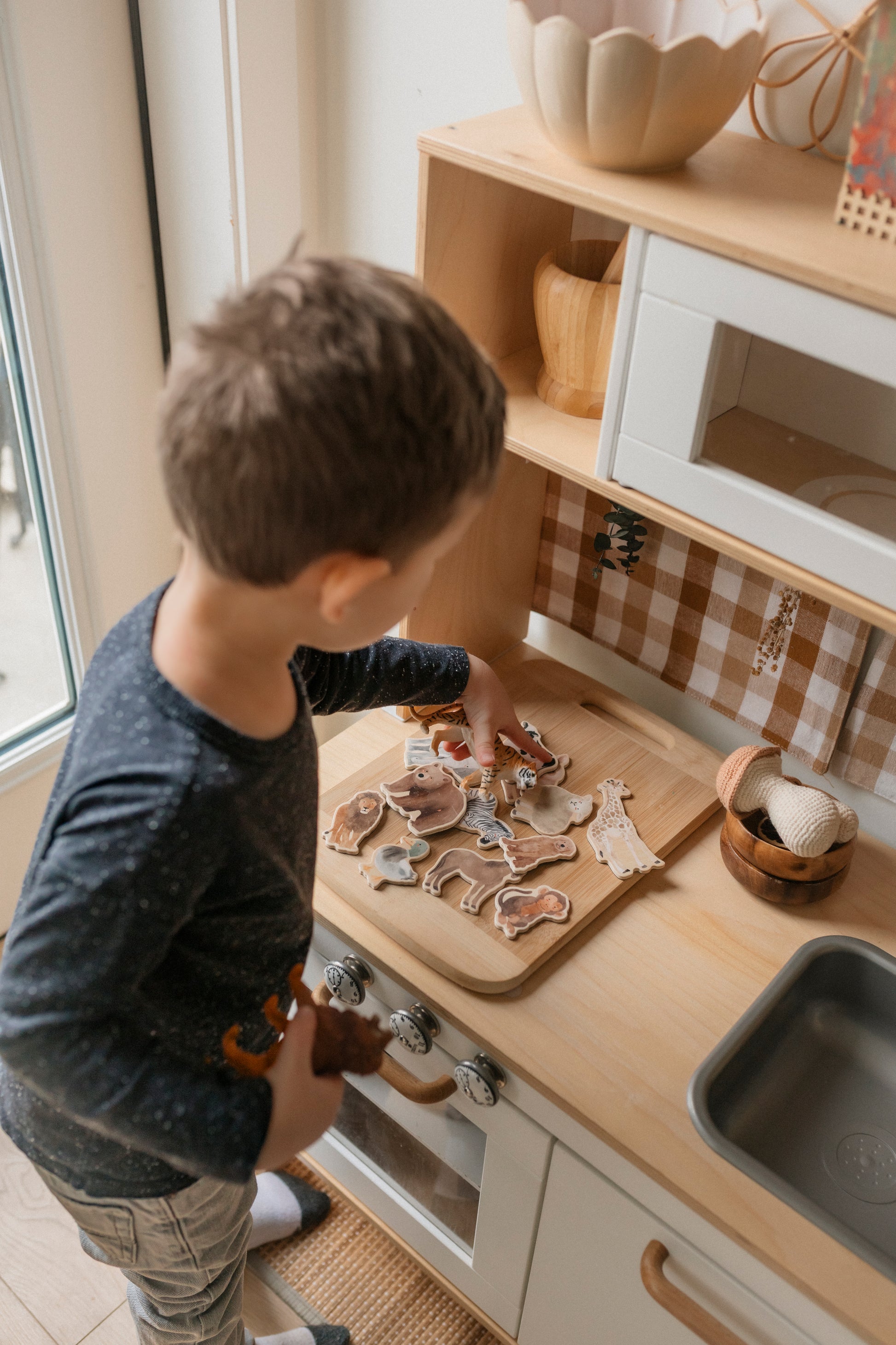 little boy playing in a kitchen with wooden animal magnets